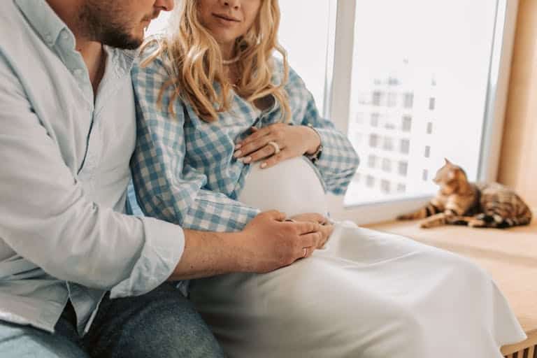 A couple enjoy a tender moment with their baby bump at home, featuring a cute cat.